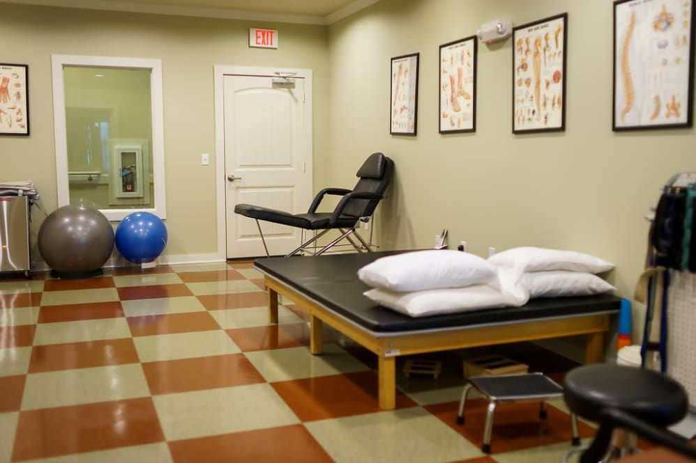 A physical therapy room with a massage table, exercise ball, and anatomical posters on the wall.