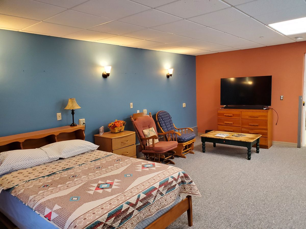 A cozy bedroom with a blue and orange accent wall, featuring a bed, chairs, and a flat-screen TV.
