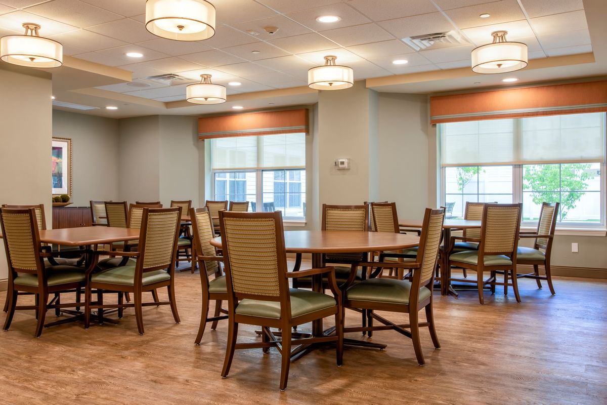 An empty dining room with neatly arranged tables and chairs, illuminated by overhead ceiling lights.