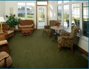 A cozy living room with upholstered chairs, a sofa, and a round table on a carpeted floor.