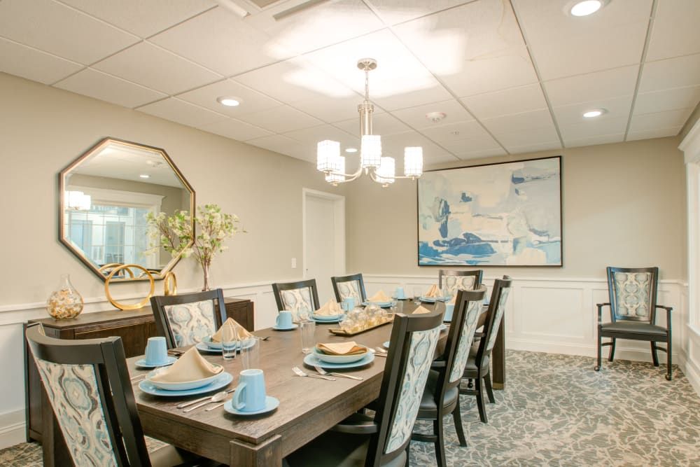 An elegantly decorated dining room with a large rectangular table set for eight, featuring modern decor and a stylish chandelier.