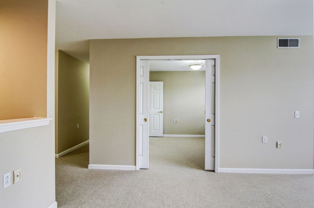 An empty room with beige walls and a carpeted floor, featuring an open doorway.