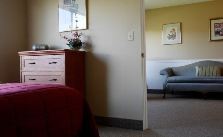 A view from a bedroom into a living room, featuring a dresser and an open doorway.