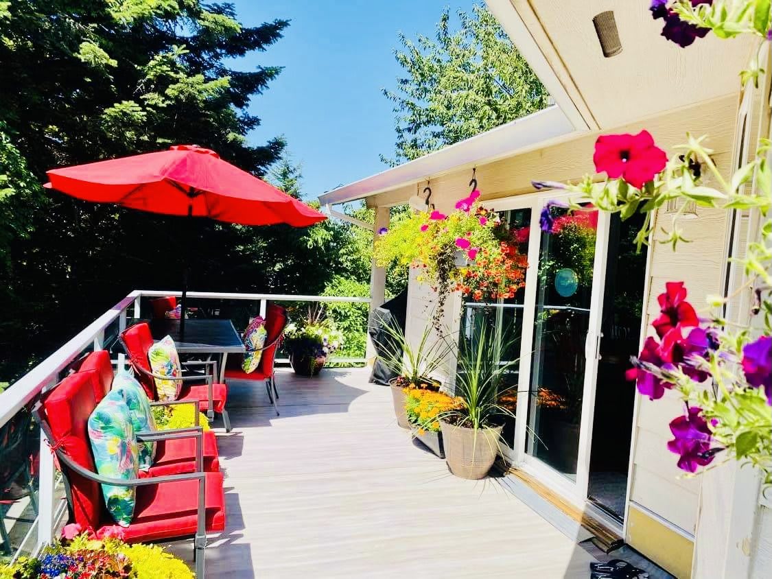 A sunny patio with vibrant flowers and comfortable seating under a red umbrella.