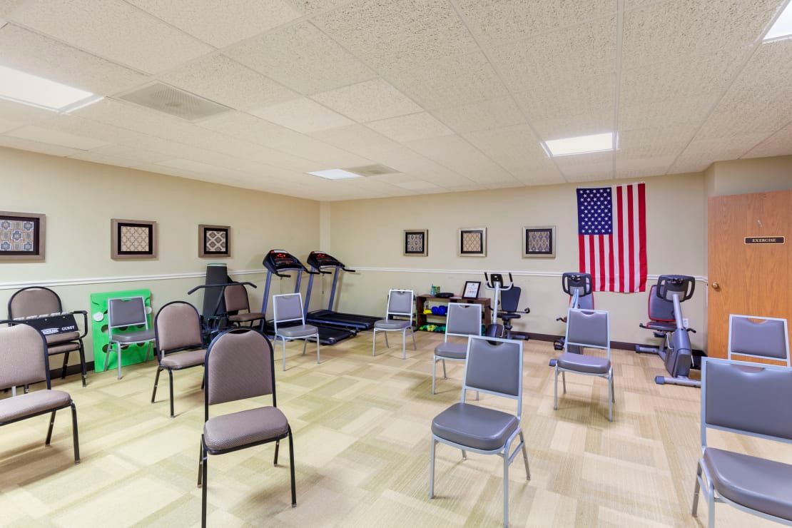 A fitness room with exercise equipment and chairs arranged for a group session.
