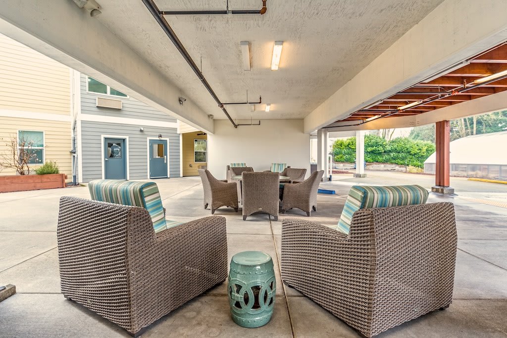 A cozy outdoor patio with rattan chairs and a decorative stool under a covered area.