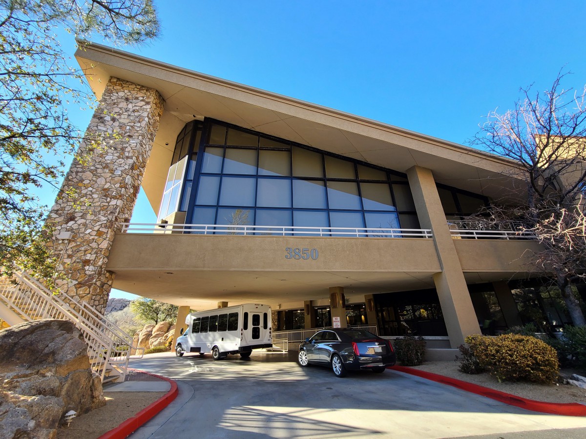 A modern building entrance with large glass windows and vehicles parked in front.