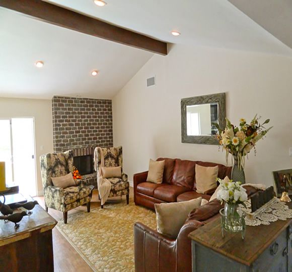A cozy living room featuring a brick fireplace, leather sofa, patterned armchairs, and a coffee table adorned with a vase of flowers.