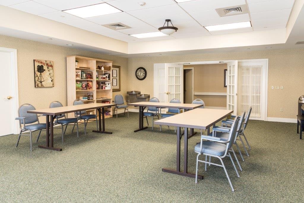 An empty meeting room with arranged tables and chairs, featuring library shelves and a clock on the wall.
