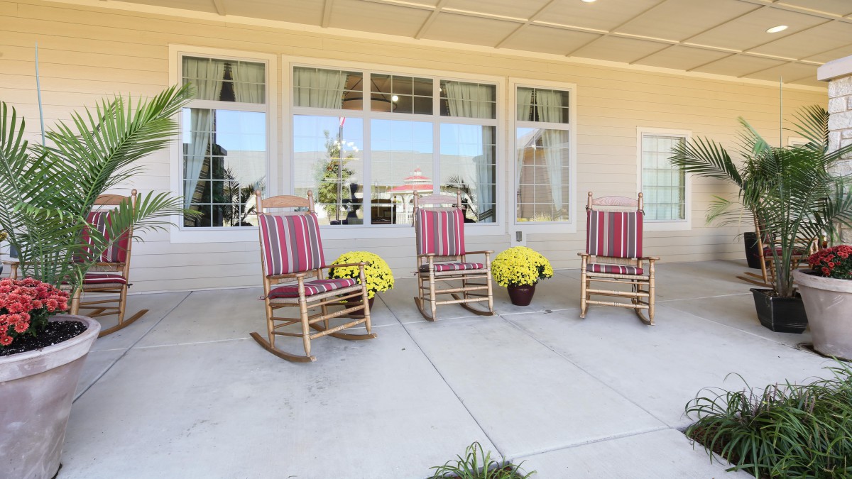 A cozy patio with three striped rocking chairs and potted yellow flowers.