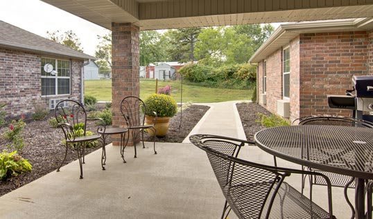 A cozy patio with metal chairs and a table, overlooking a landscaped walkway.