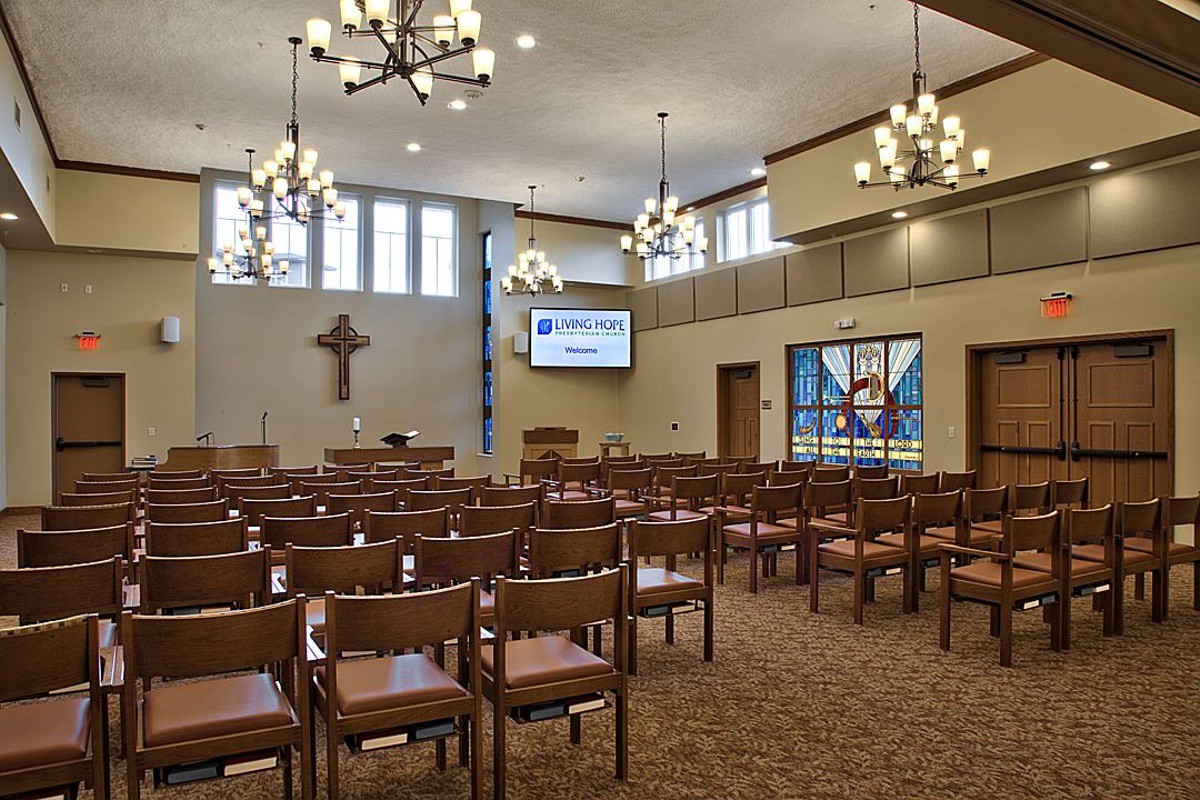 An interior view of a chapel with rows of chairs, chandeliers, and stained glass windows.