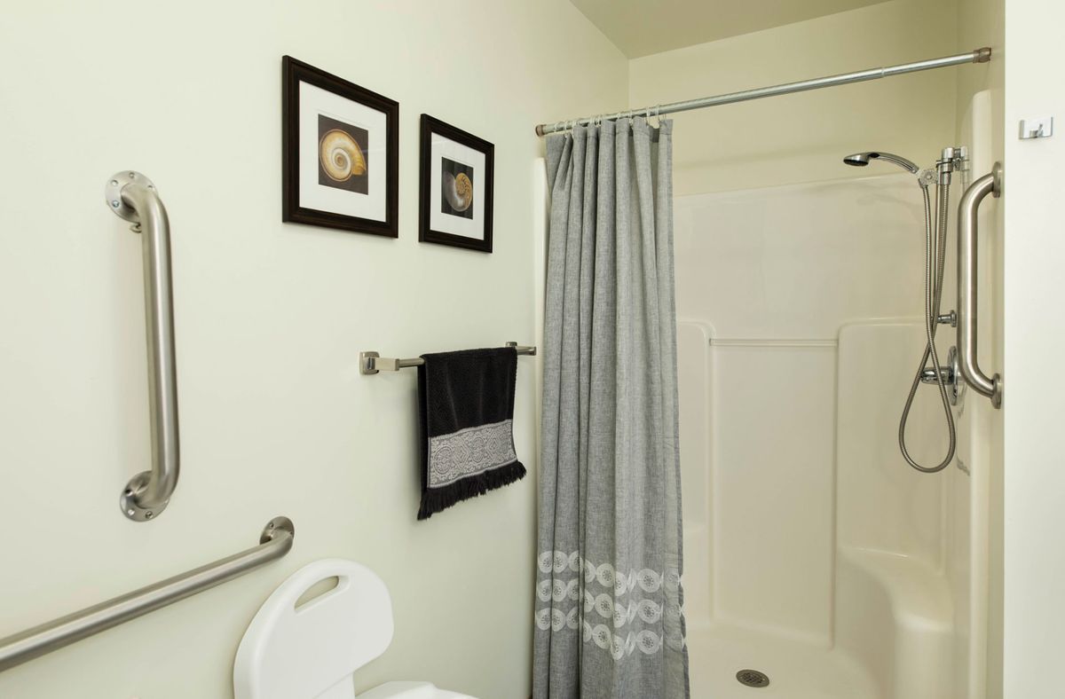 A small bathroom featuring a shower with a gray curtain, framed art on the wall, and a towel hanging on a rack.