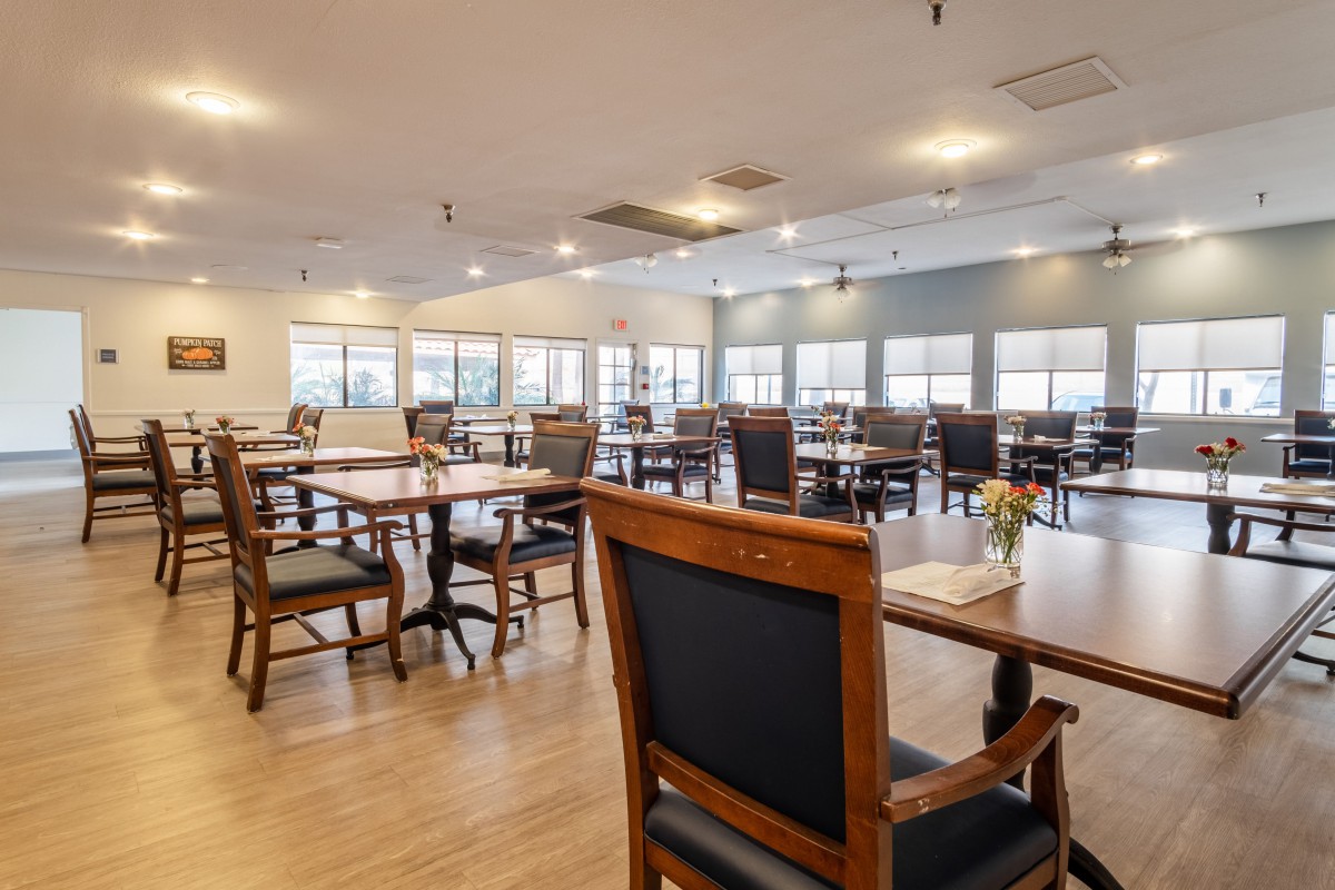 An empty dining room with wooden tables and chairs, softly lit by overhead lights.