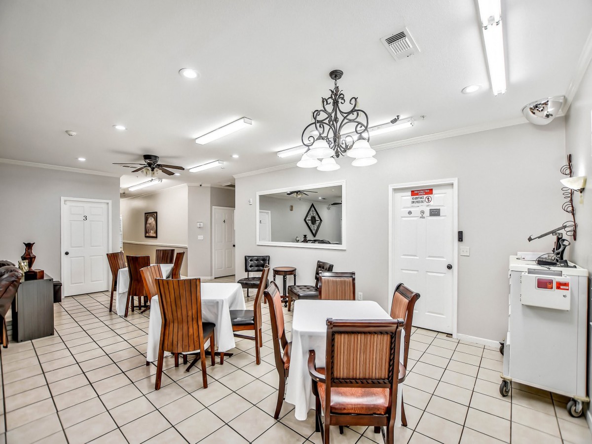 A well-lit dining area with multiple tables and chairs, featuring a chandelier and tiled flooring.