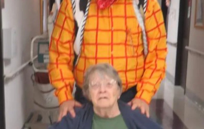 An elderly woman is seated in front of a person wearing a plaid shirt and a red bandana.