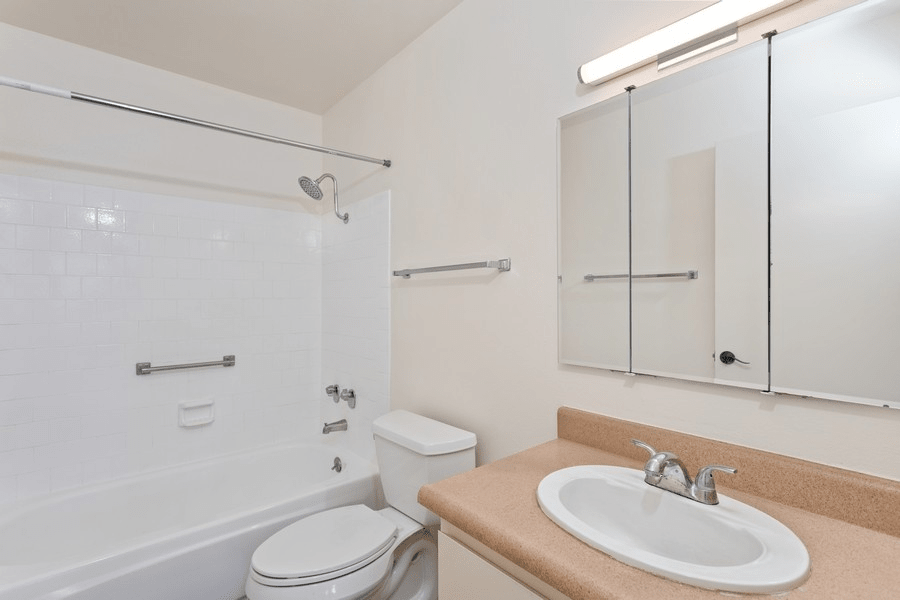 A modern bathroom featuring a bathtub with a shower, a sink with a mirror cabinet, and white walls.