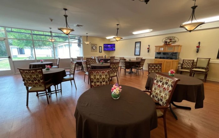 A cozy dining area with elegantly arranged tables and chairs, featuring flower centerpieces and warm lighting.