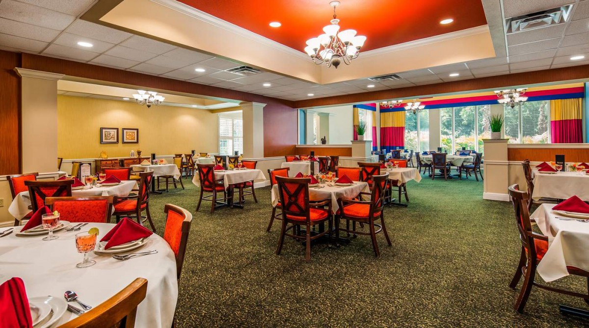 An elegantly designed restaurant dining area with neatly arranged tables and chairs, showcasing warm lighting and a carpeted floor.