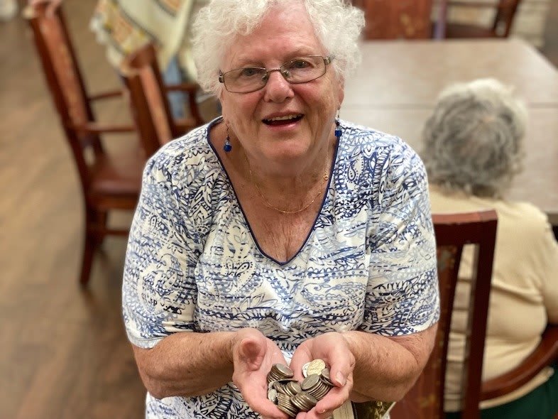 An elderly woman with white hair smiling and holding something in her hands indoors.