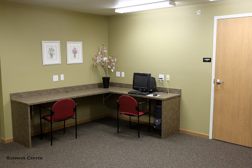 A tidy office workspace featuring a desk with a computer and two red chairs, set against green walls.