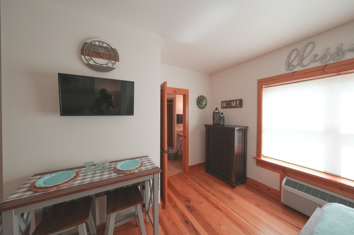 A cozy dining area with a table and two chairs, a wall-mounted television, and natural light from a window.