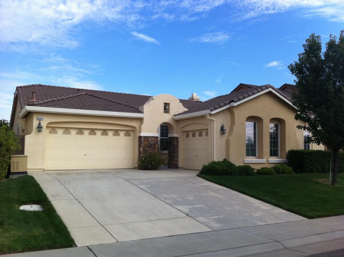 A suburban residential house with a two-car garage and a driveway, under a clear blue sky.