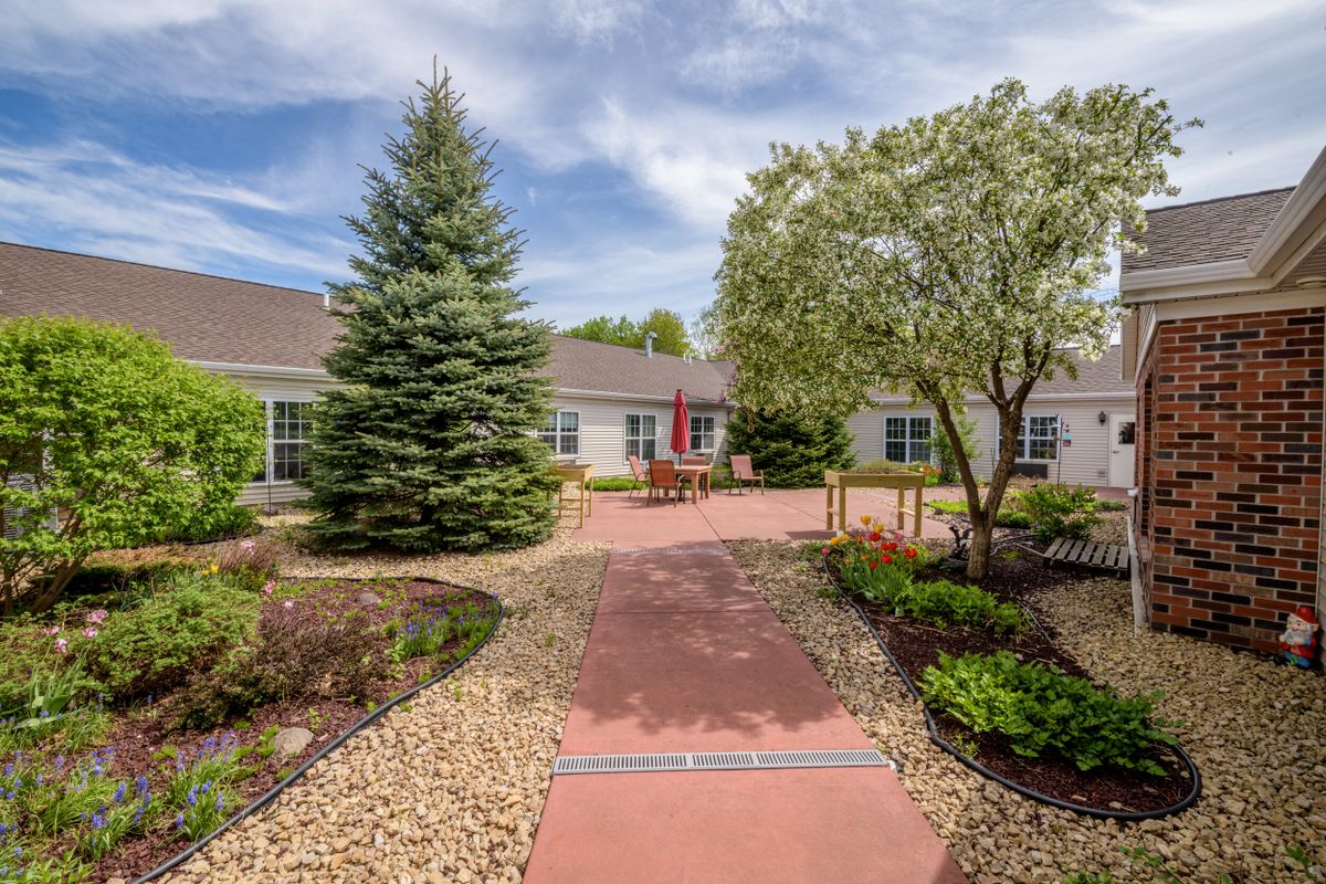 A beautifully landscaped pathway leading to a house, surrounded by lush trees and gardens under a clear sky.