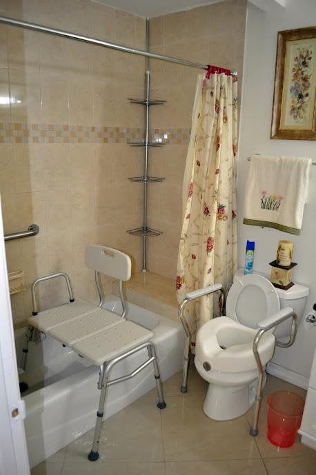 A bathroom equipped with an accessible shower and toilet, featuring safety rails and a bath chair.