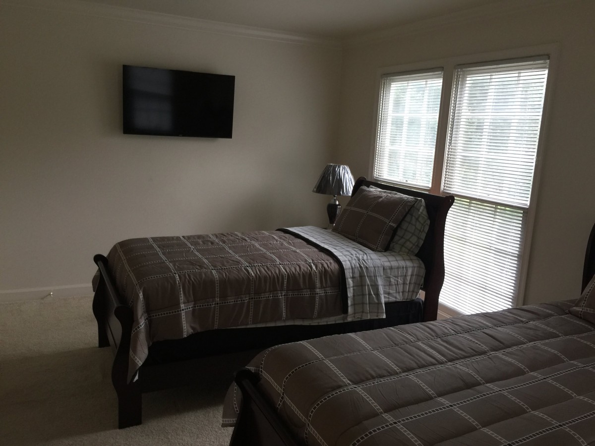 A cozy bedroom with two twin beds, a wall-mounted television, and large windows letting in natural light.