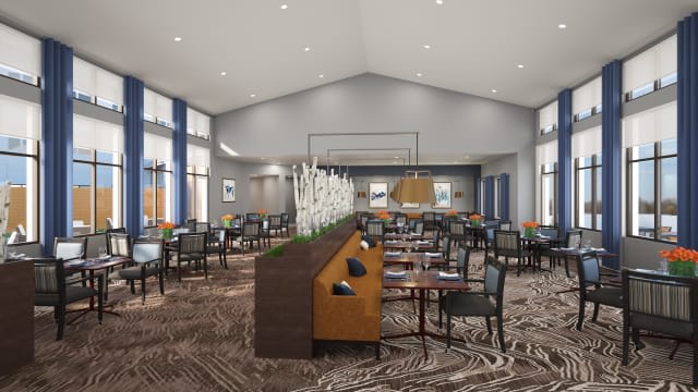 A modern restaurant dining area with neatly arranged tables and chairs, featuring decorative lighting and carpeted flooring.