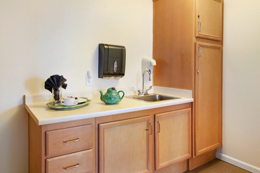 A small kitchenette with wooden cabinets, a sink, and a teapot on the countertop.