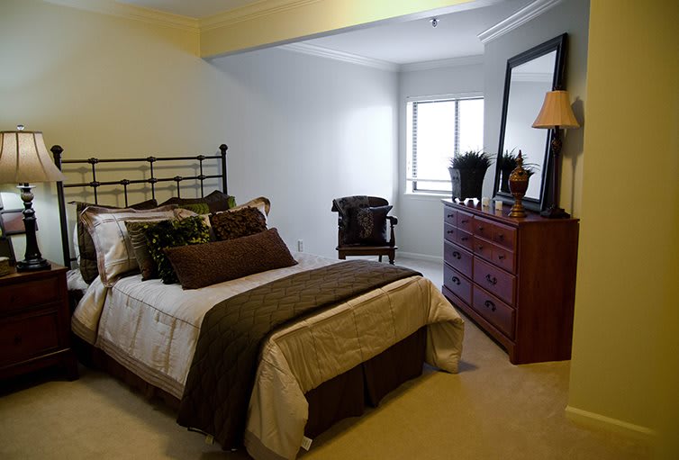 A cozy bedroom with a neatly made bed, dresser, and chair by the window.