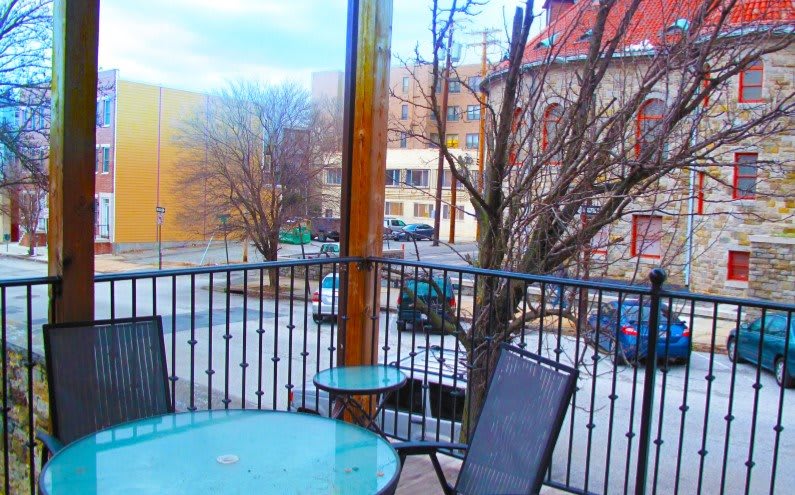 A cozy outdoor patio with chairs and a table overlooking an urban street scene.