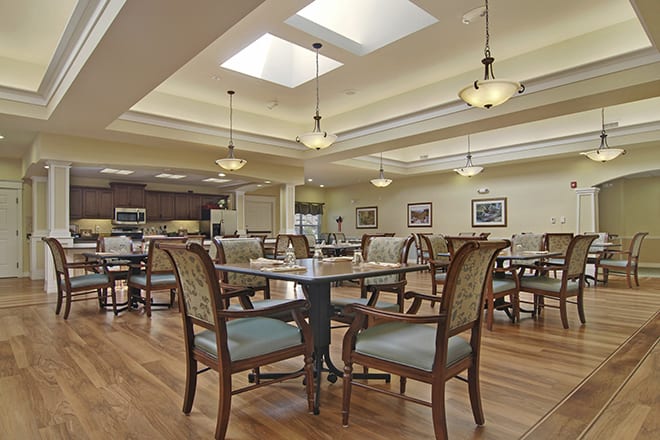 A spacious dining room with elegant tables and chairs arranged under warm lighting and skylights.