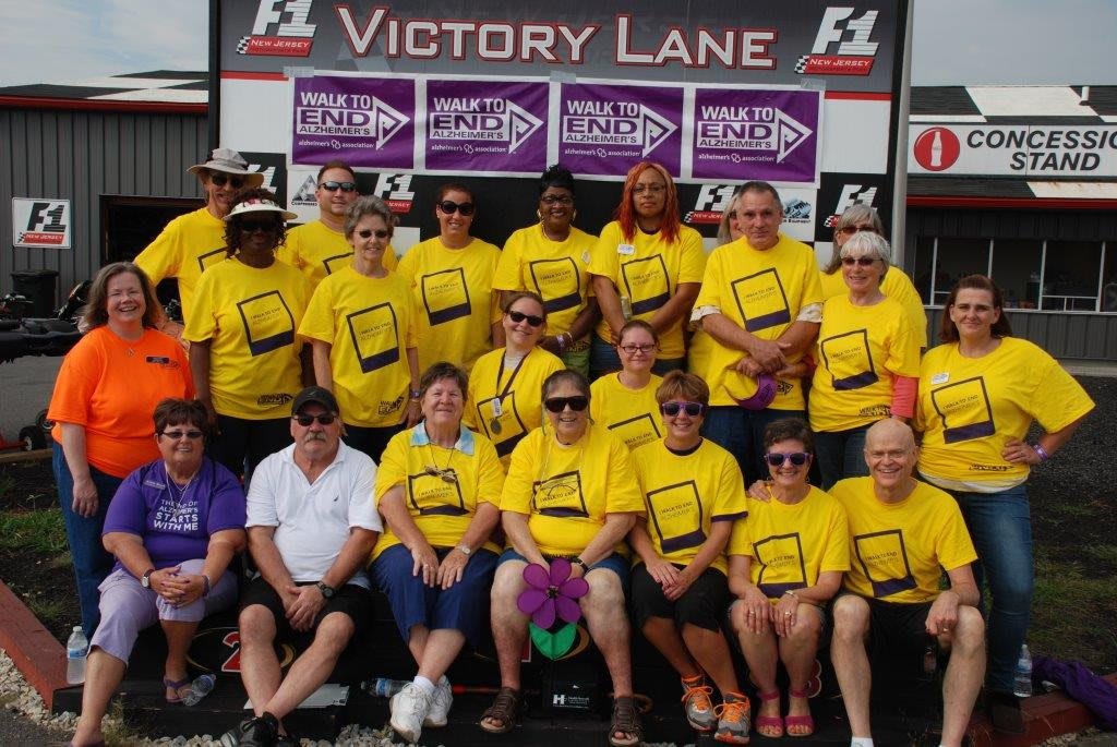A group of people wearing yellow shirts pose for a team photo at Victory Lane.
