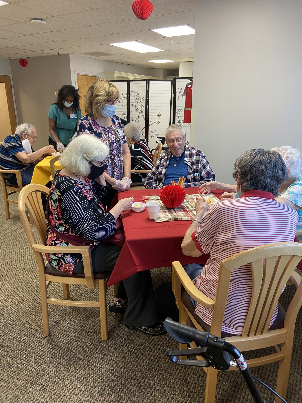 A group of seniors seated around a table, engaging in conversation at an indoor gathering.