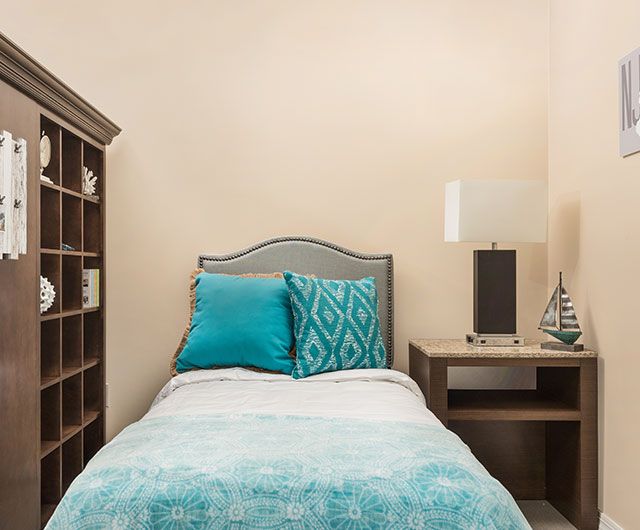 A cozy bedroom featuring a single bed with turquoise bedding, a bookshelf, and a nightstand with a lamp.