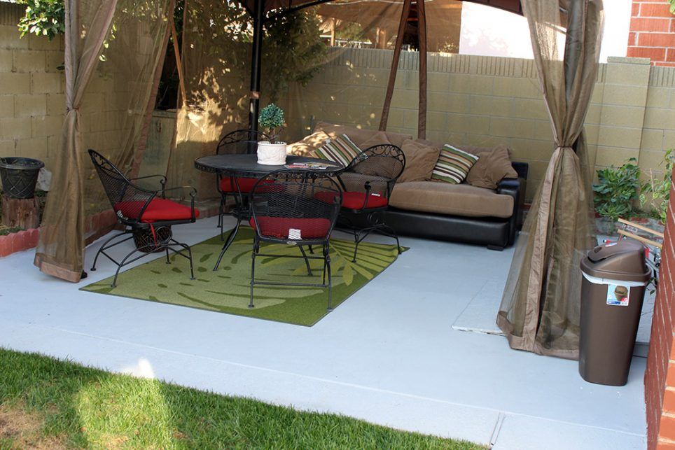 A cozy outdoor patio setup with a sofa, chairs, table, and a green rug under a canopy.