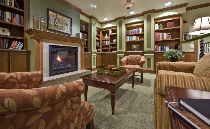 A cozy library room featuring a fireplace, comfortable seating, and bookshelves filled with books.
