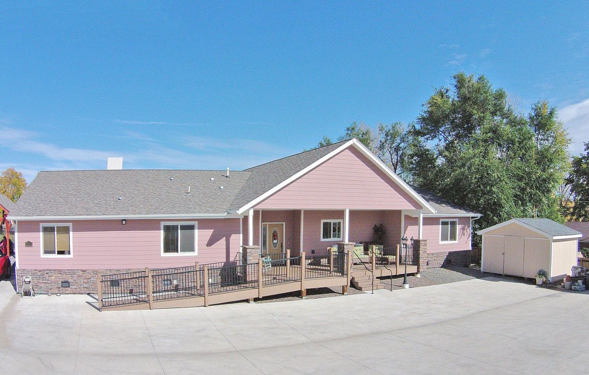 A pink suburban house with a front porch and driveway, surrounded by trees on a clear day.