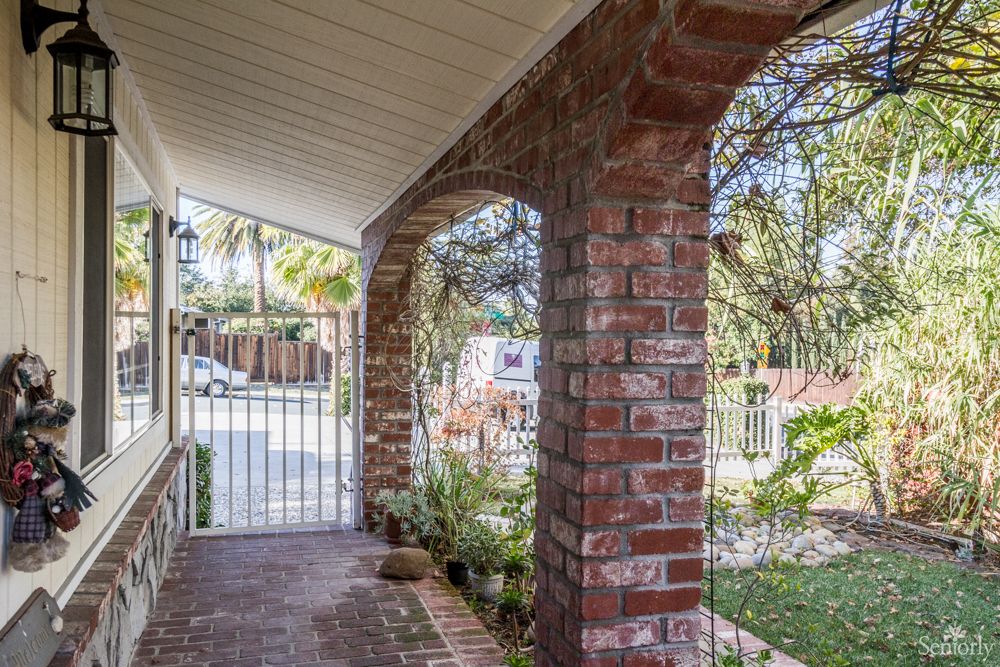 A brick porch with arches, overlooking a garden with a gated entrance.