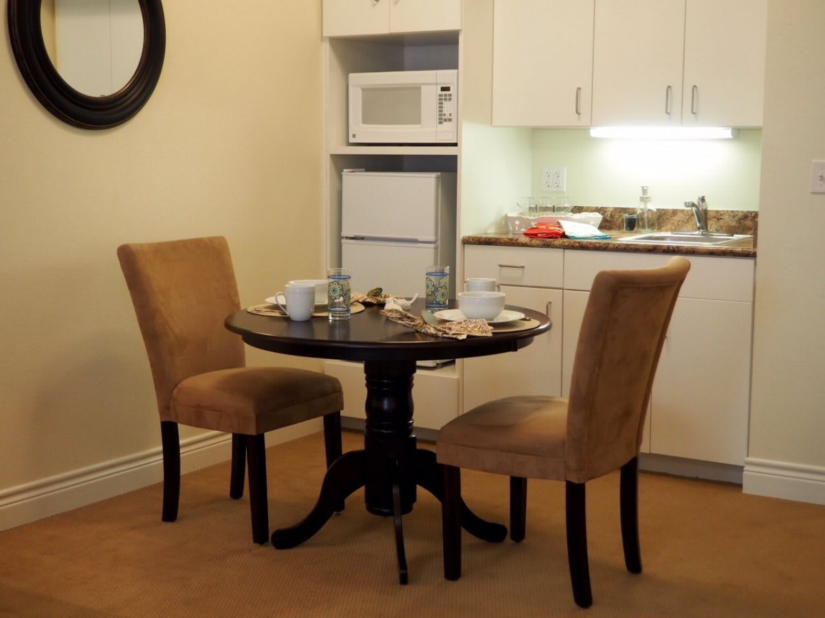 A cozy dining area with a small round table and two chairs, adjacent to a kitchenette equipped with a microwave and refrigerator.