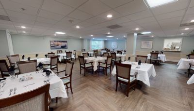 A spacious, elegantly decorated restaurant dining room with white tablecloths and neatly arranged chairs.