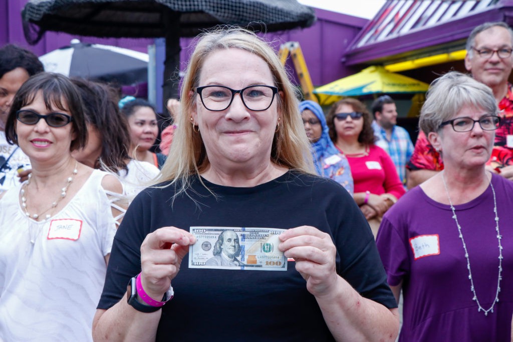 A woman holding a banknote in front of a crowd at an outdoor event.
