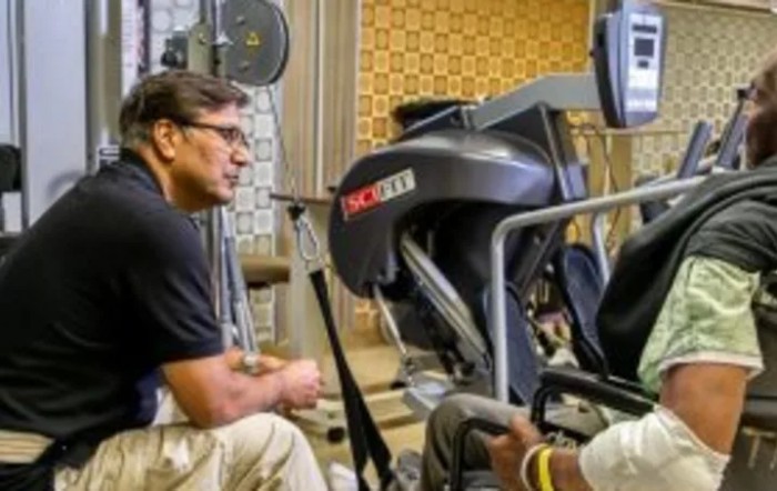 A trainer interacting with a person using exercise equipment in a gym setting.