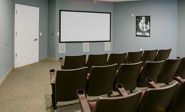 A small home theater room with rows of chairs facing a blank projector screen.