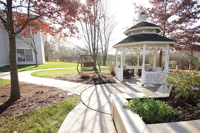 A scenic garden featuring a gazebo, swing, and winding pathways under a clear sky.