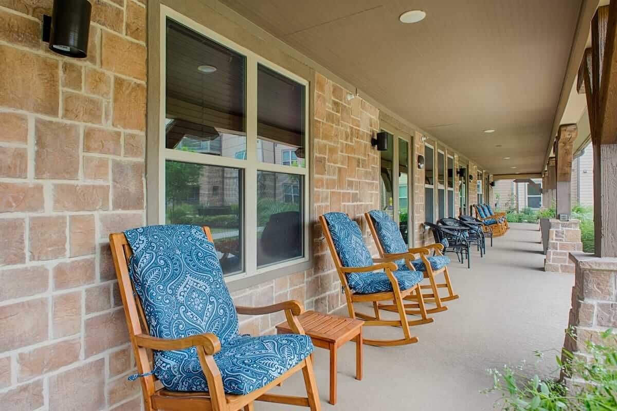A cozy porch featuring wooden rocking chairs with blue patterned cushions along a brick wall.