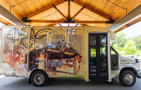 A shuttle bus with lodge-themed advertising parked under a wooden canopy.